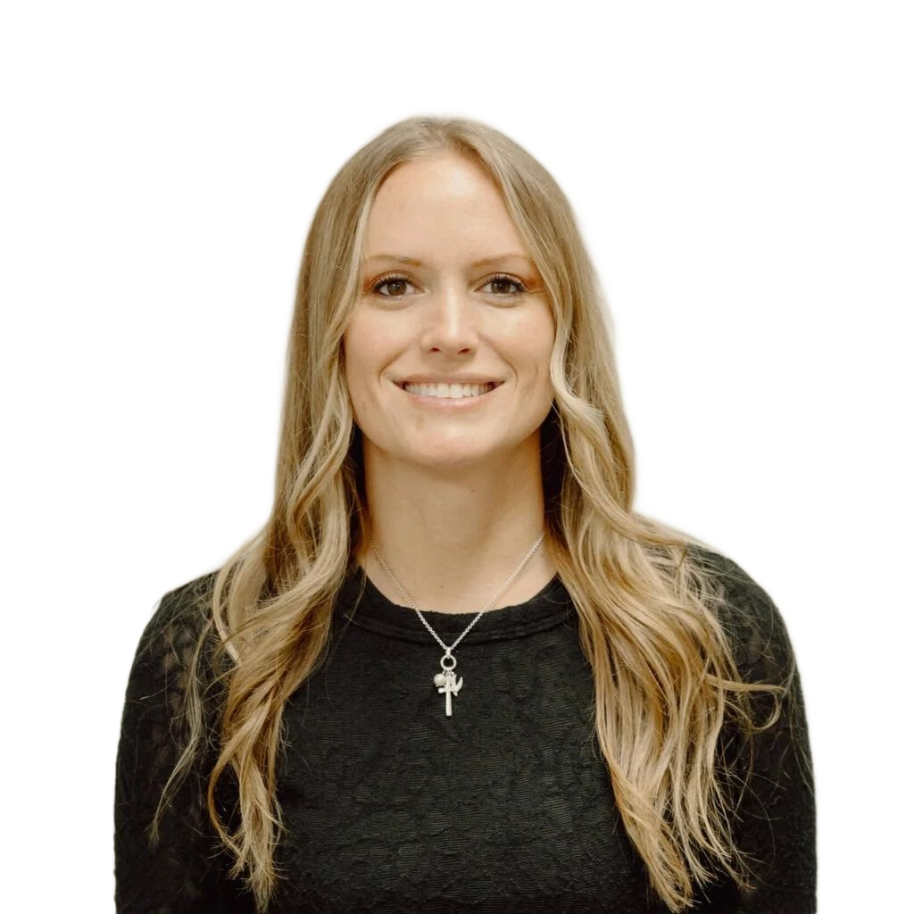 Woman with long blonde hair smiles at the camera, wearing a dark sweater and a silver pendant, set against a neutral wall.