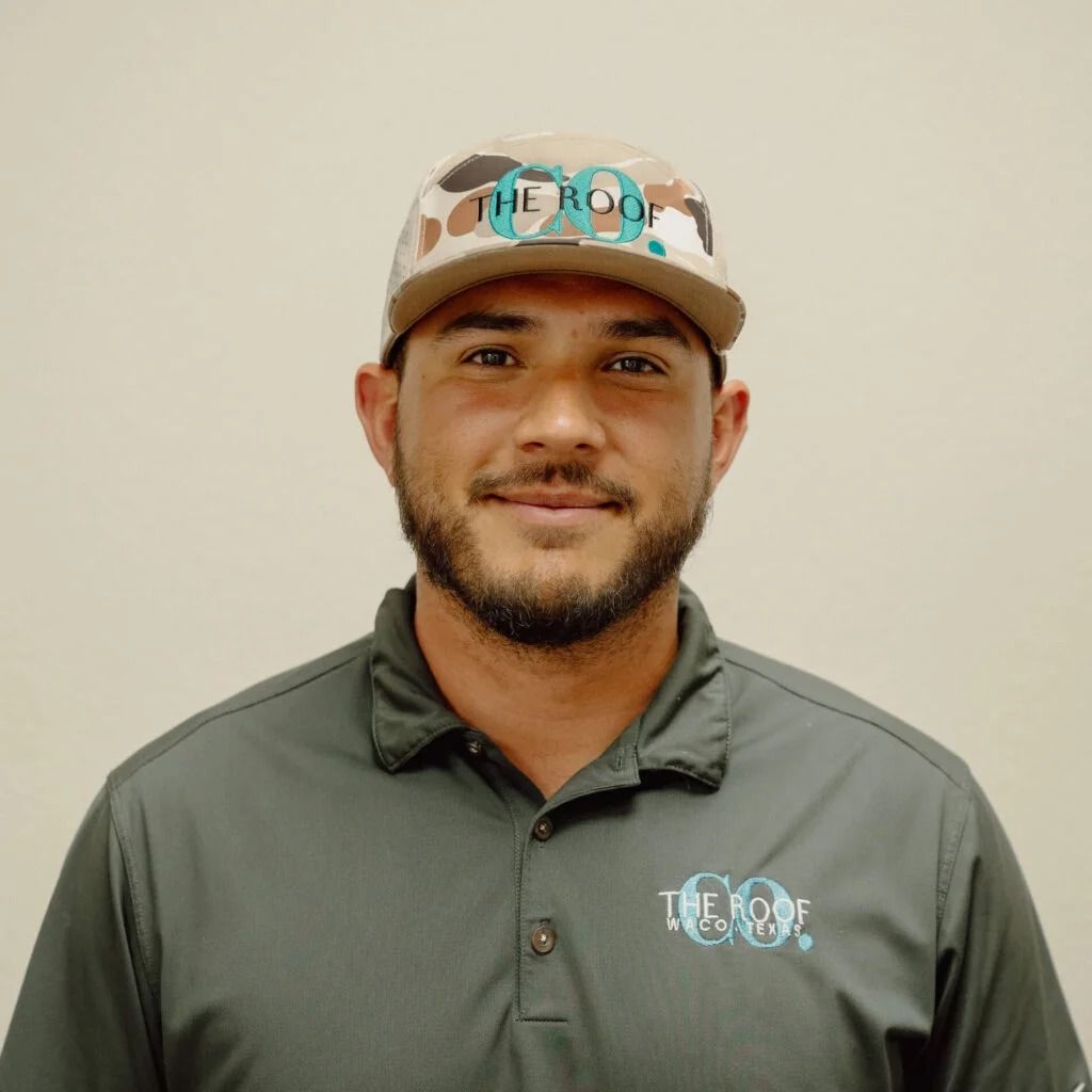 A man wearing a camouflage baseball cap and gray polo shirt, smiling at the camera. He has a beard and the logo 