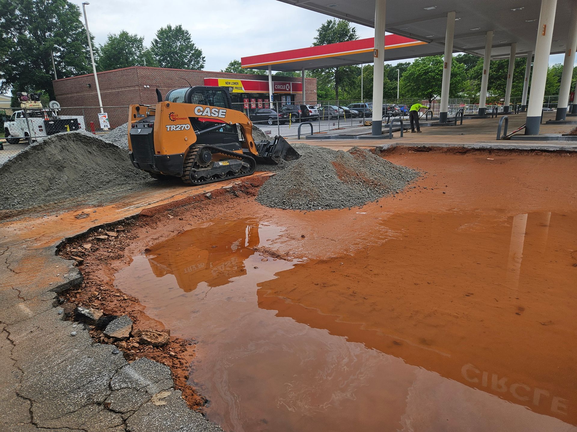 A bulldozer is working on a hole in the ground in front of a gas station.