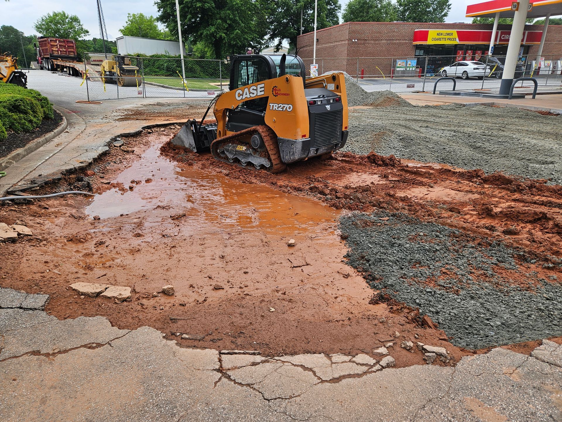A bulldozer is digging a hole in the ground in front of a gas station.