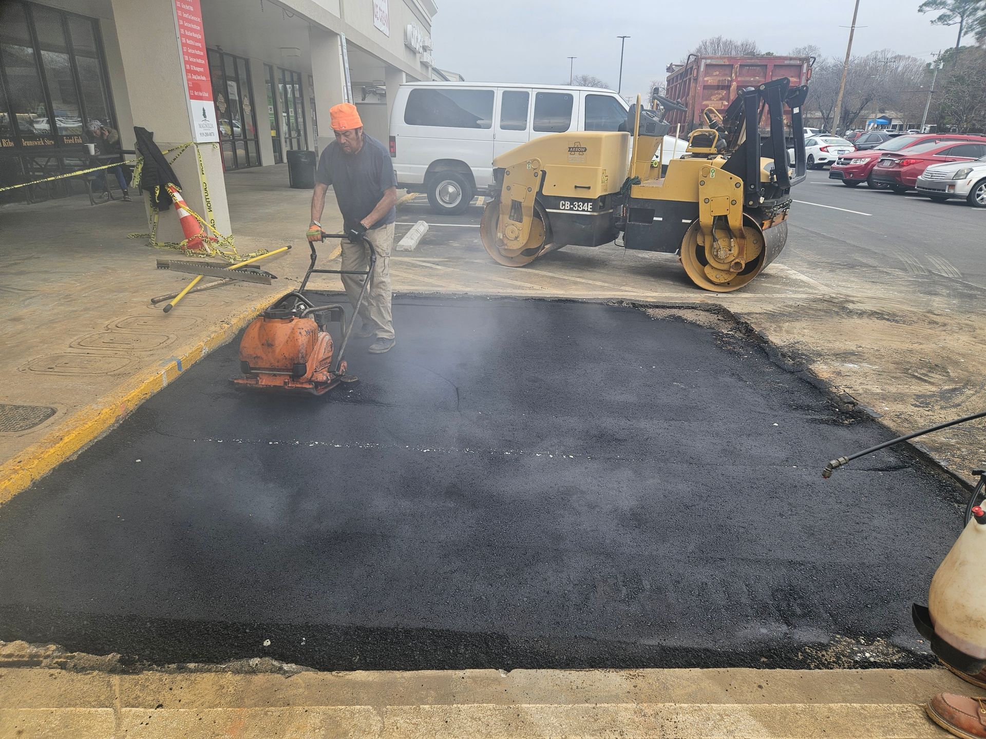 A man is using a machine to spread asphalt in a parking lot.