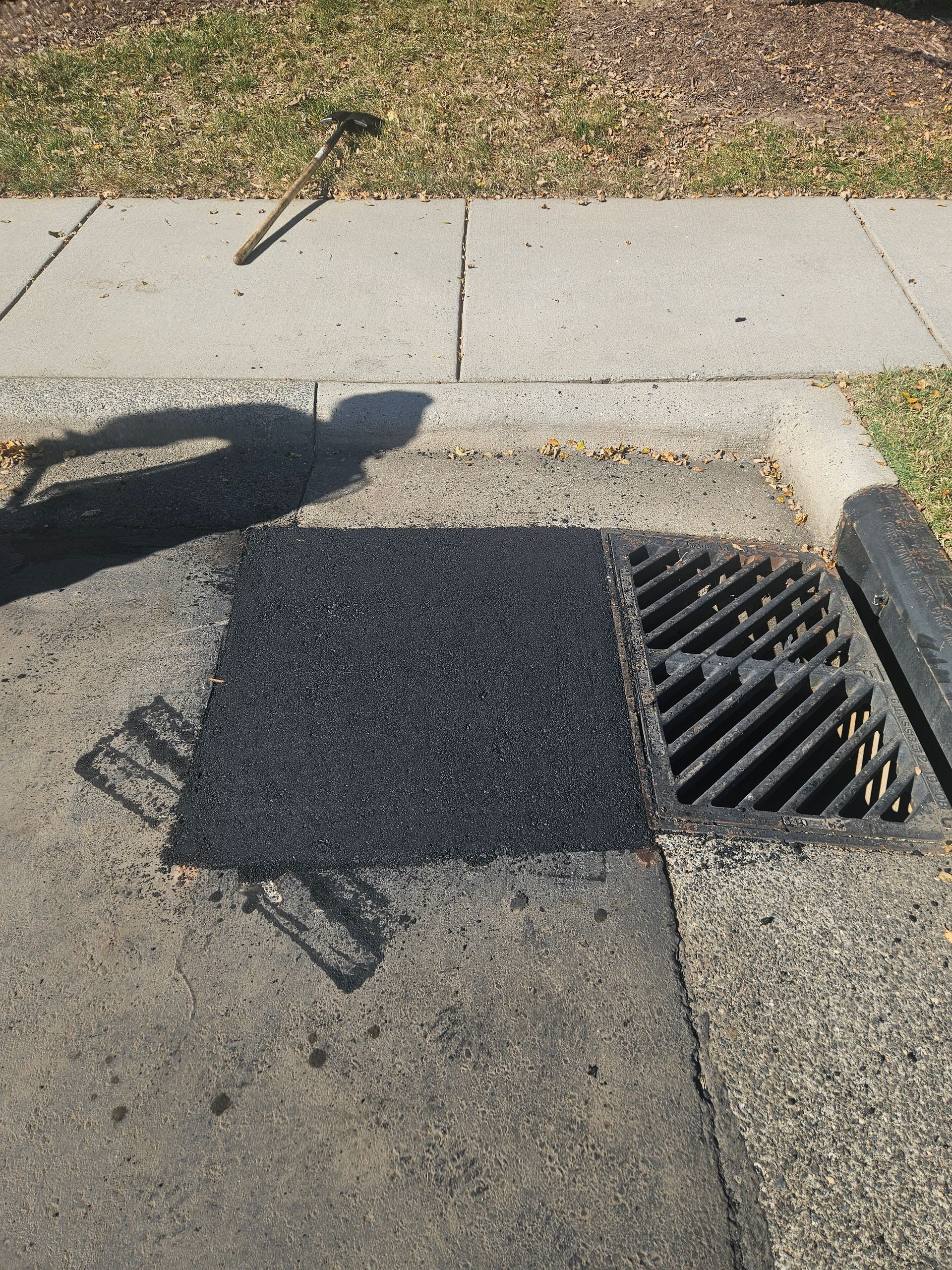 A drain on the sidewalk has been patched with black asphalt.