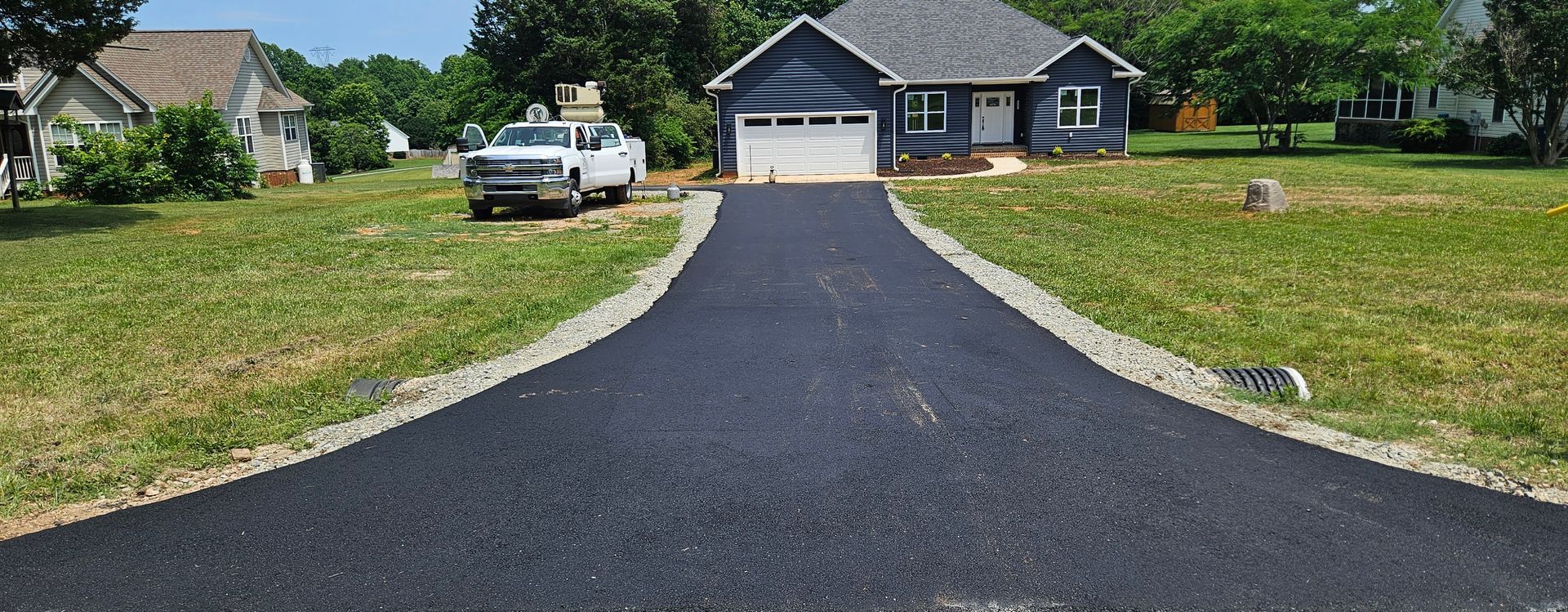 A black driveway leading to a blue house with a white truck parked in front of it.
