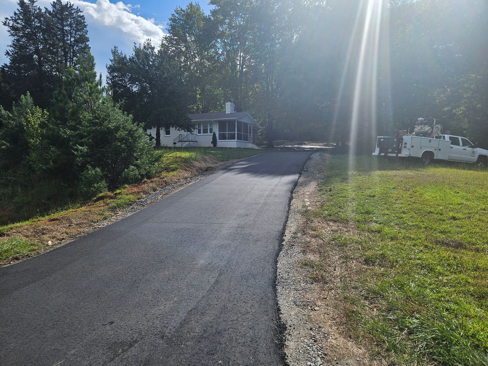 A white truck is parked on the side of an asphalt road next to a house.