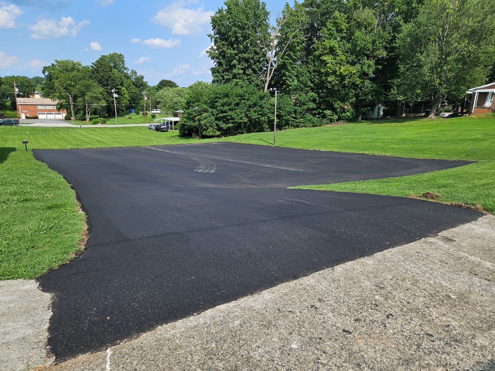 A black asphalt driveway is surrounded by grass and trees.