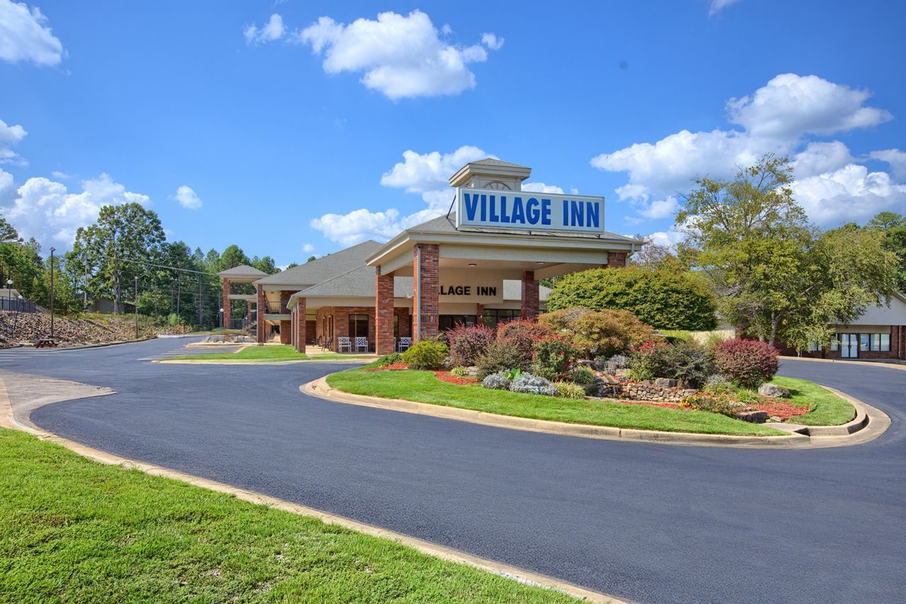 Village Inn motel with a circular drive, blue sky, and green landscaping.