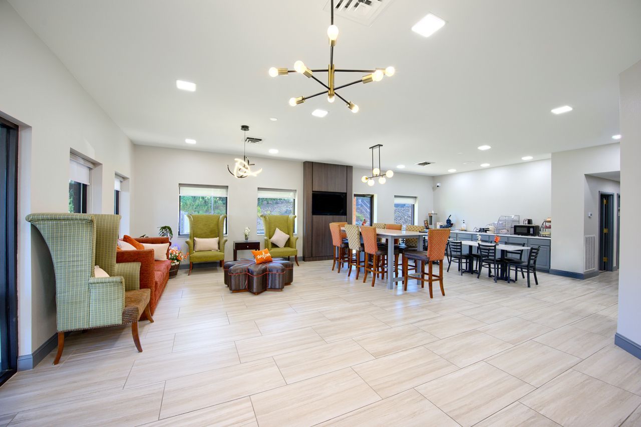 Spacious lounge with seating, dining area, and neutral tones. Modern chandelier hangs above.