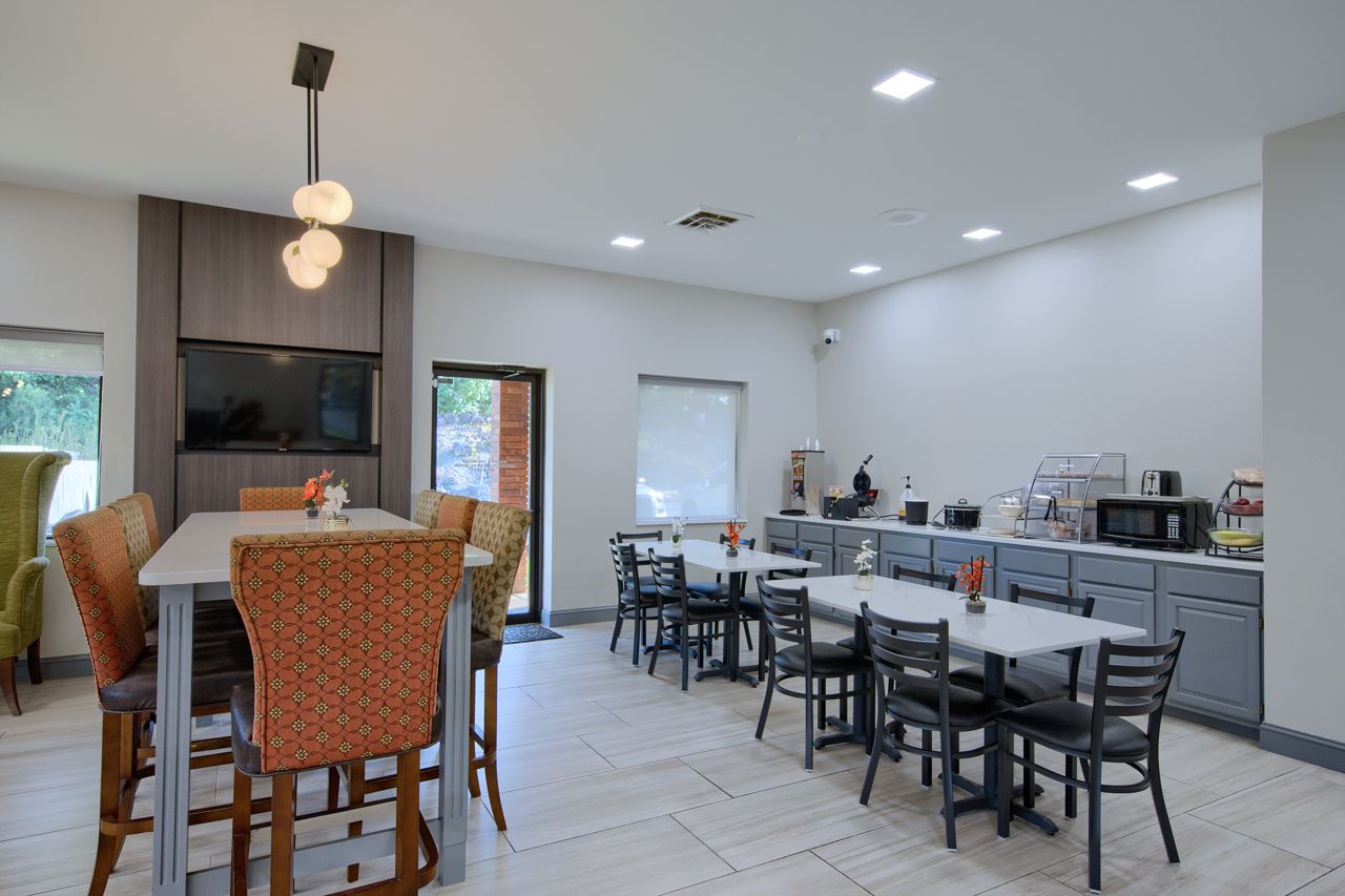 Hotel breakfast area with tables, chairs, and buffet. Neutral walls, modern decor.