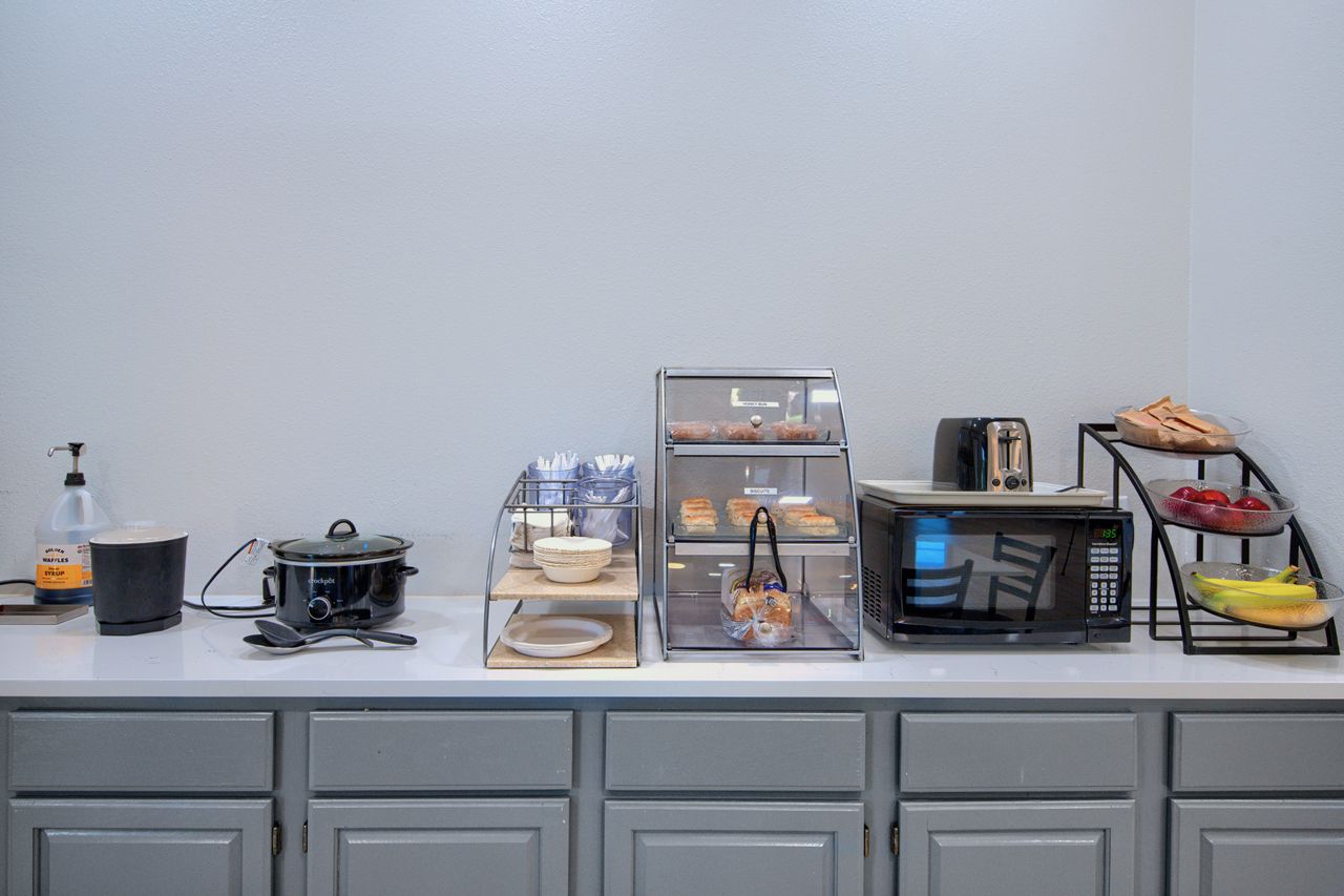 A hotel breakfast buffet with various appliances, food, and cabinets set against a plain wall.