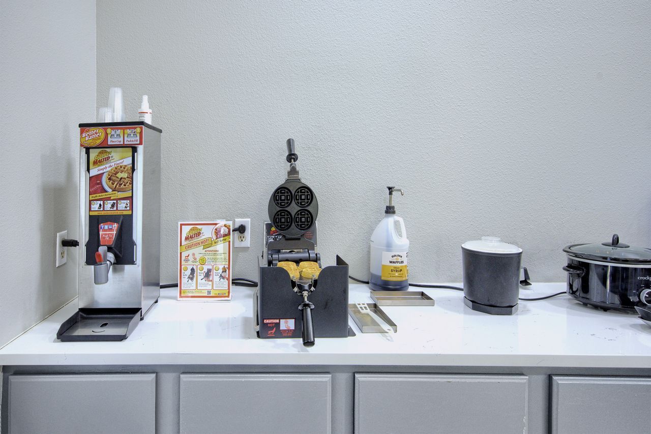 Breakfast bar with a waffle maker, coffee dispenser, and other food preparation items.