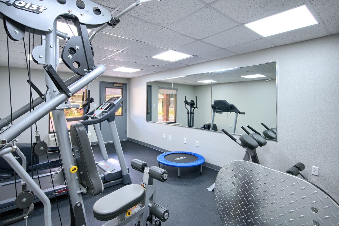 Gym with weight machines, treadmill, elliptical, and small trampoline. Large mirror on wall.