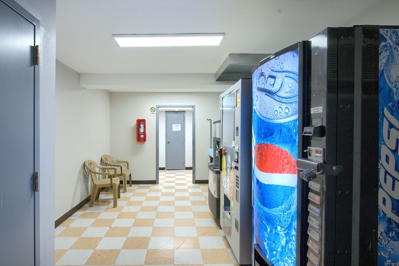 Hallway with vending machines, checkered floor, fire extinguisher, and chairs.