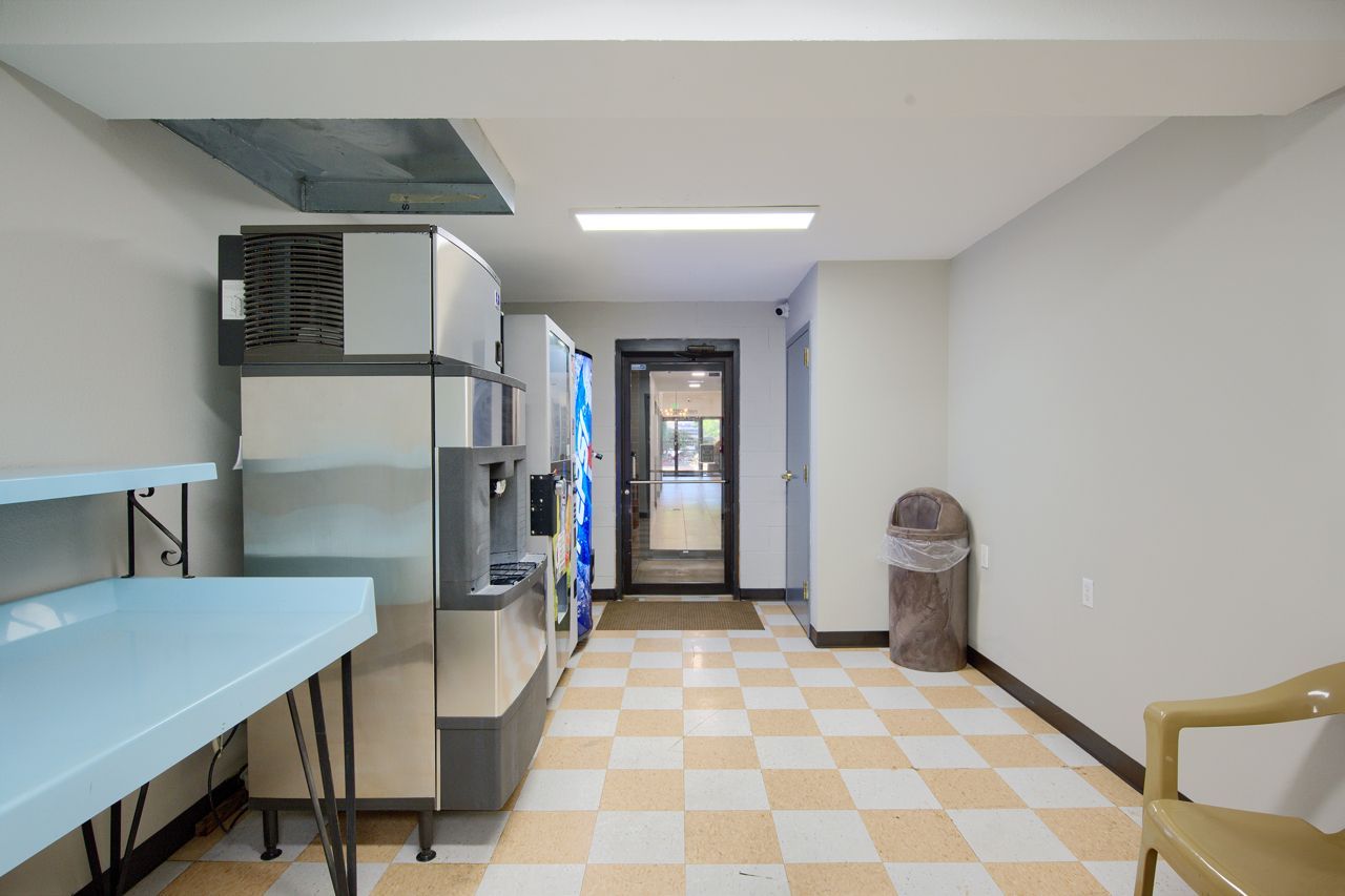 Hallway with vending machines, blue counter, trash can, checkered floor, and door.