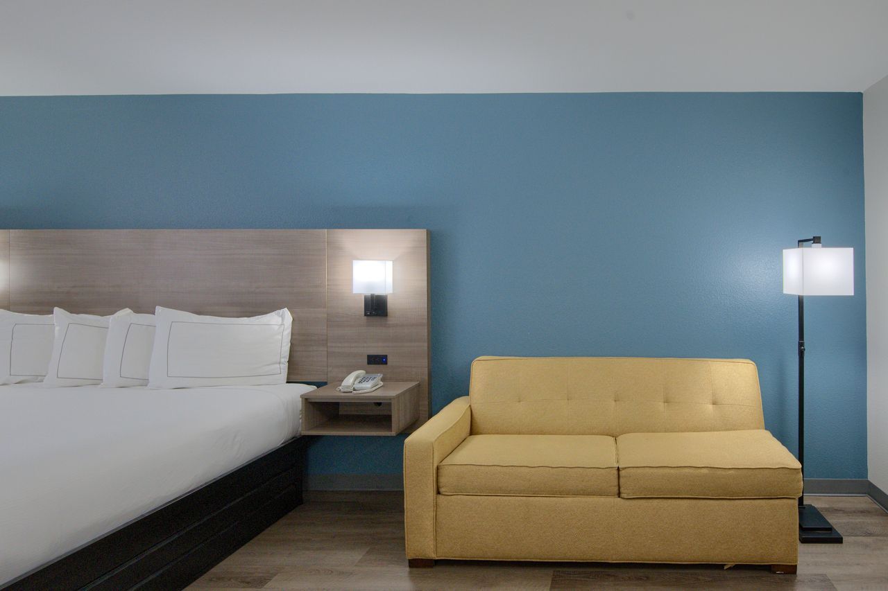 Hotel room with bed, sofa, lamp, and blue wall.