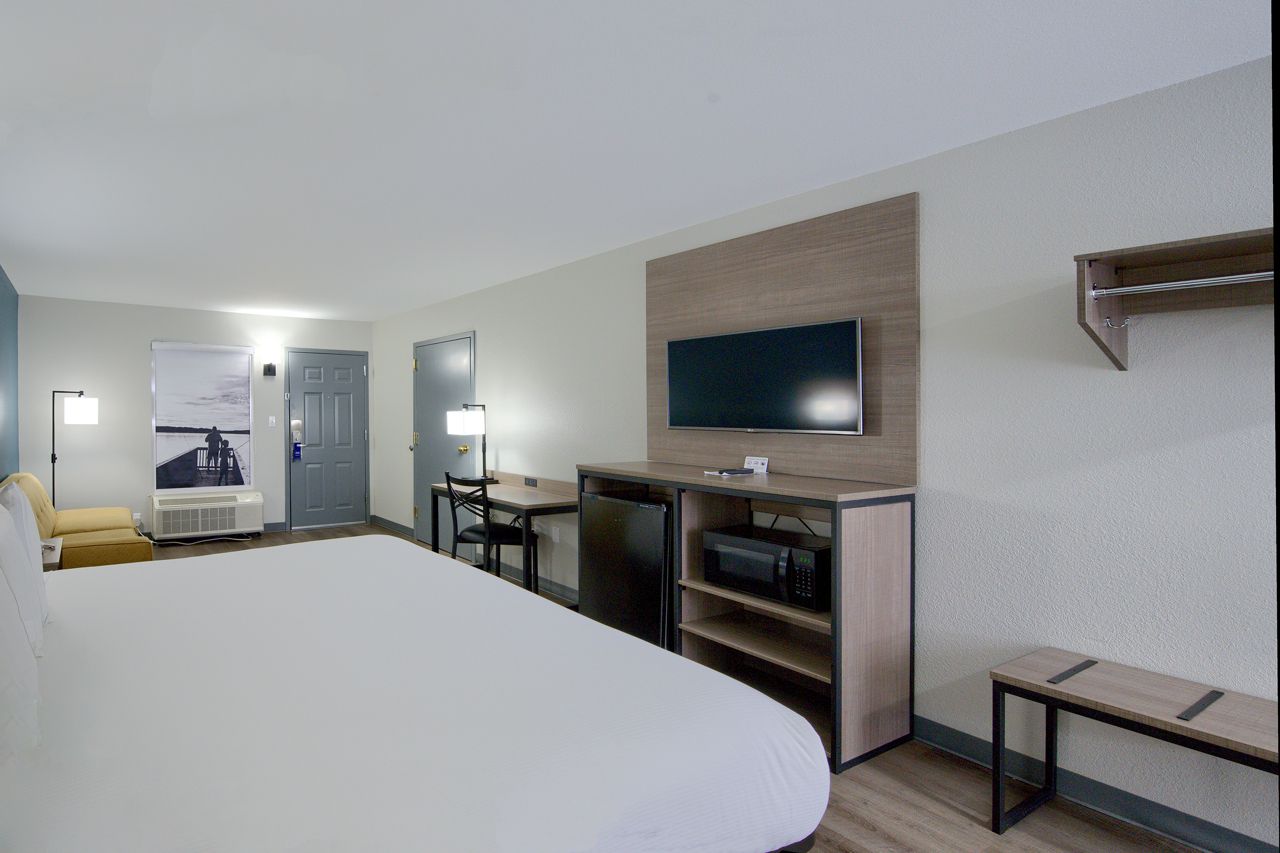 Hotel room with a bed, TV, desk, and amenities. Neutral tones, well-lit.