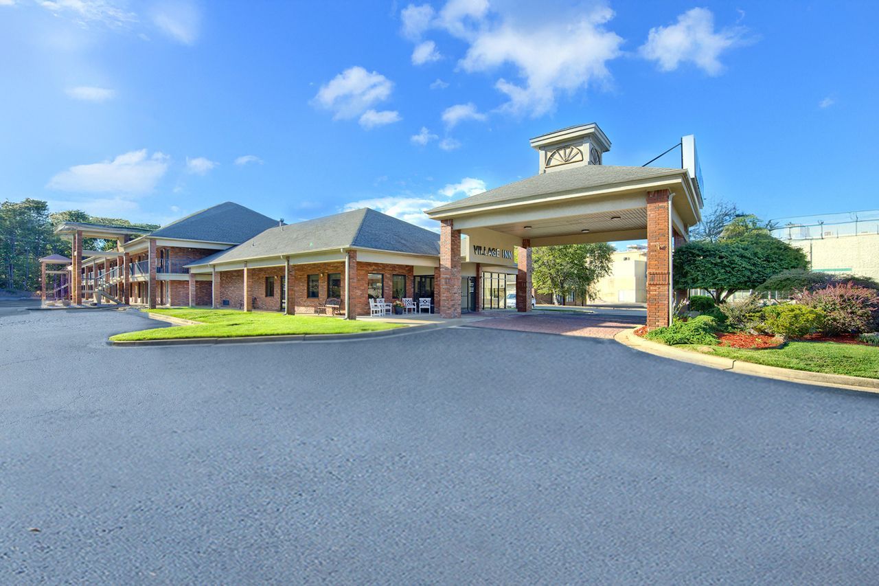 Village Inn hotel entrance with red brick, beige accents, and blue sky.