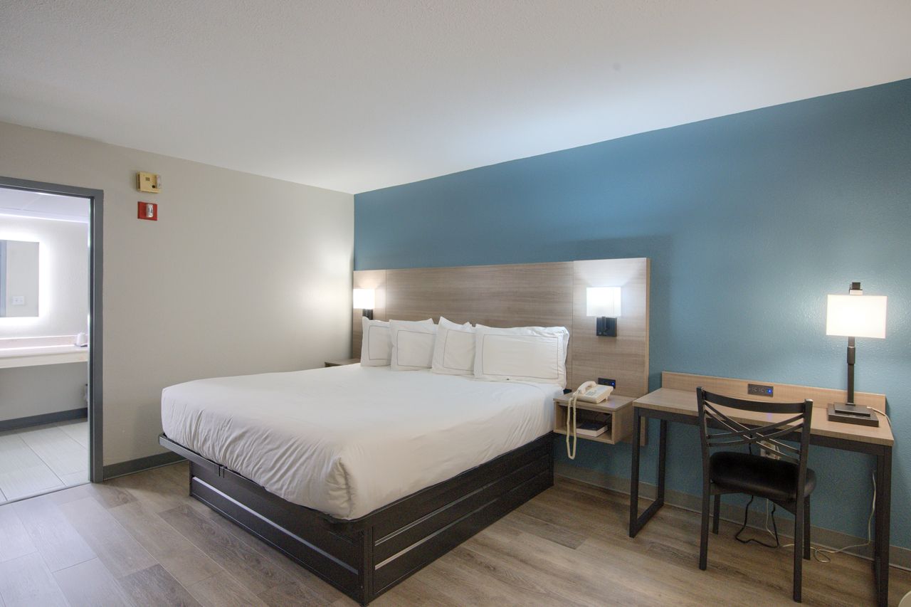 Hotel room with a queen bed, desk, and bathroom visible in the background.
