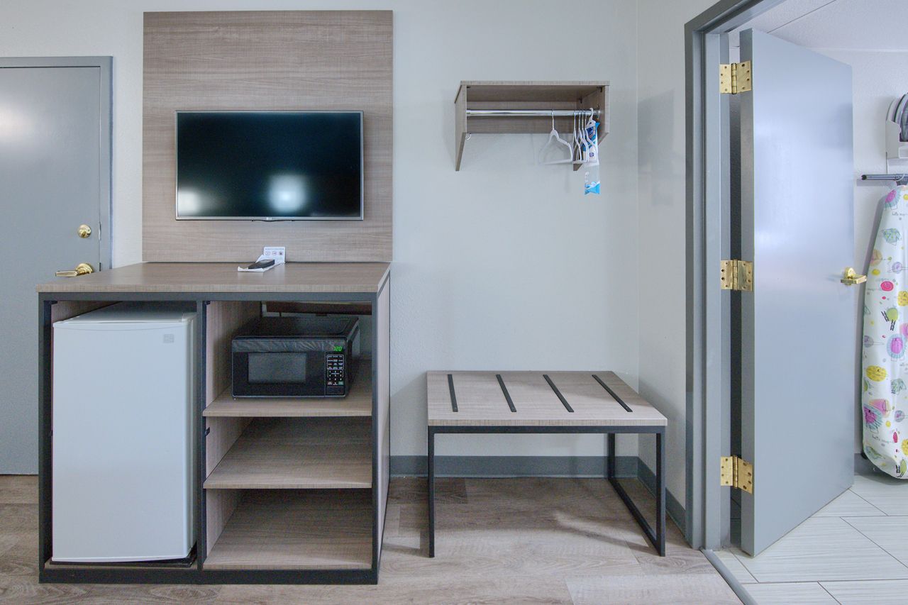 Hotel room with TV, microwave, refrigerator, bench, closet entrance.