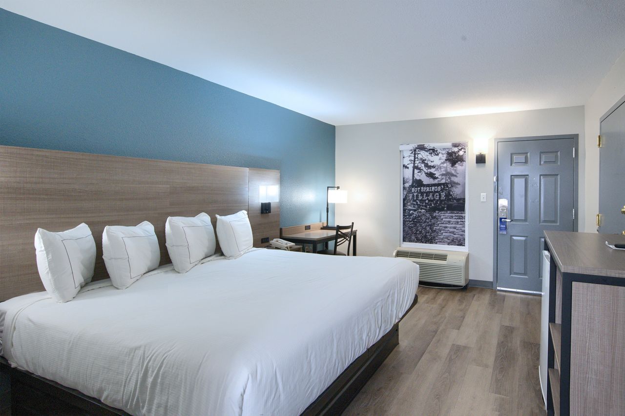 Hotel room with king bed, blue accent wall, wooden floors, table, and dresser.