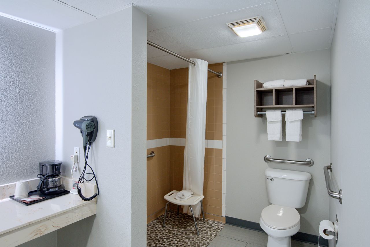 Hotel bathroom, accessible shower, toilet with grab bars, towels, coffee maker.