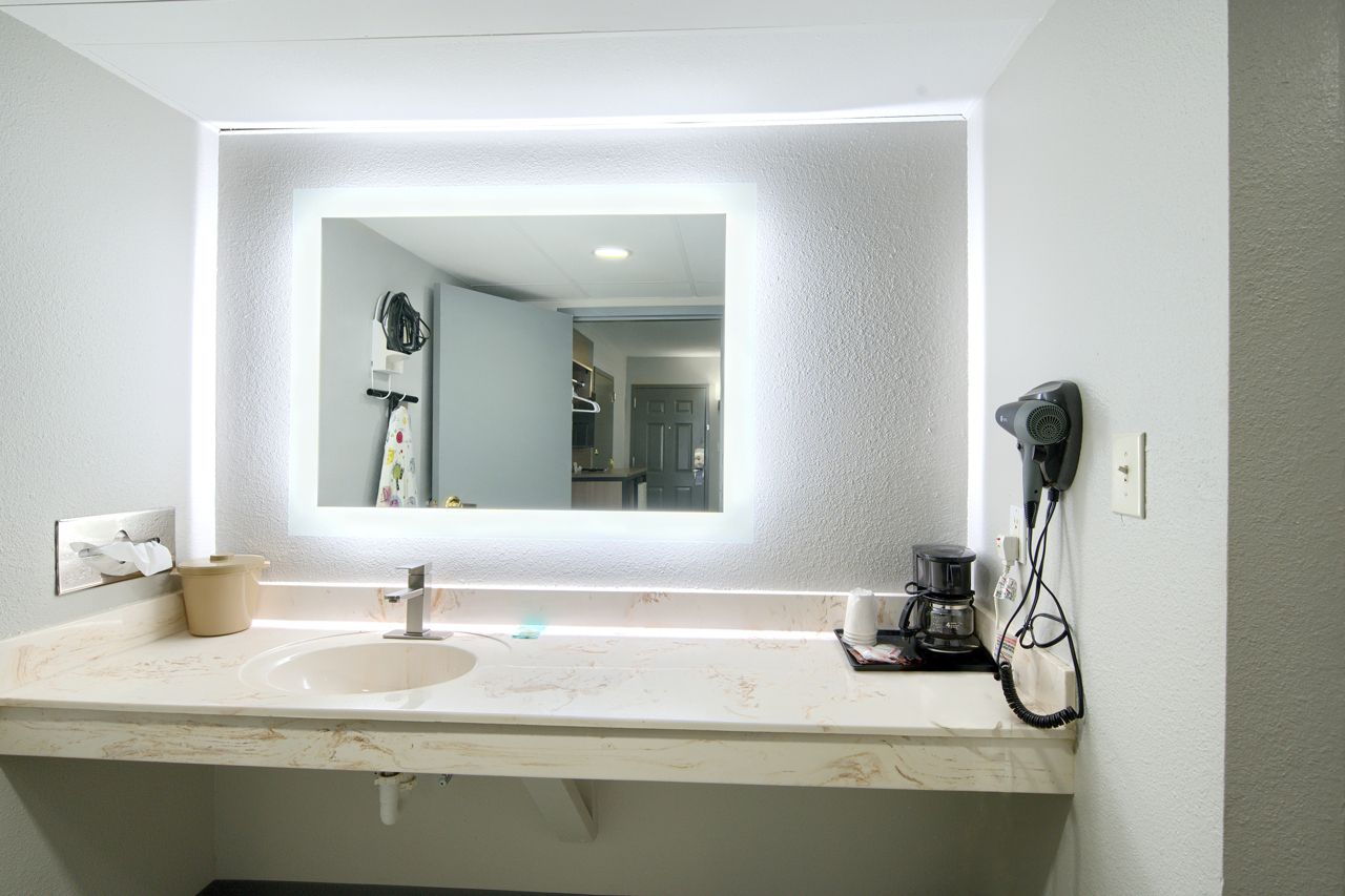 Bathroom with lit mirror, sink, and countertop. Hair dryer and coffee maker on the counter.
