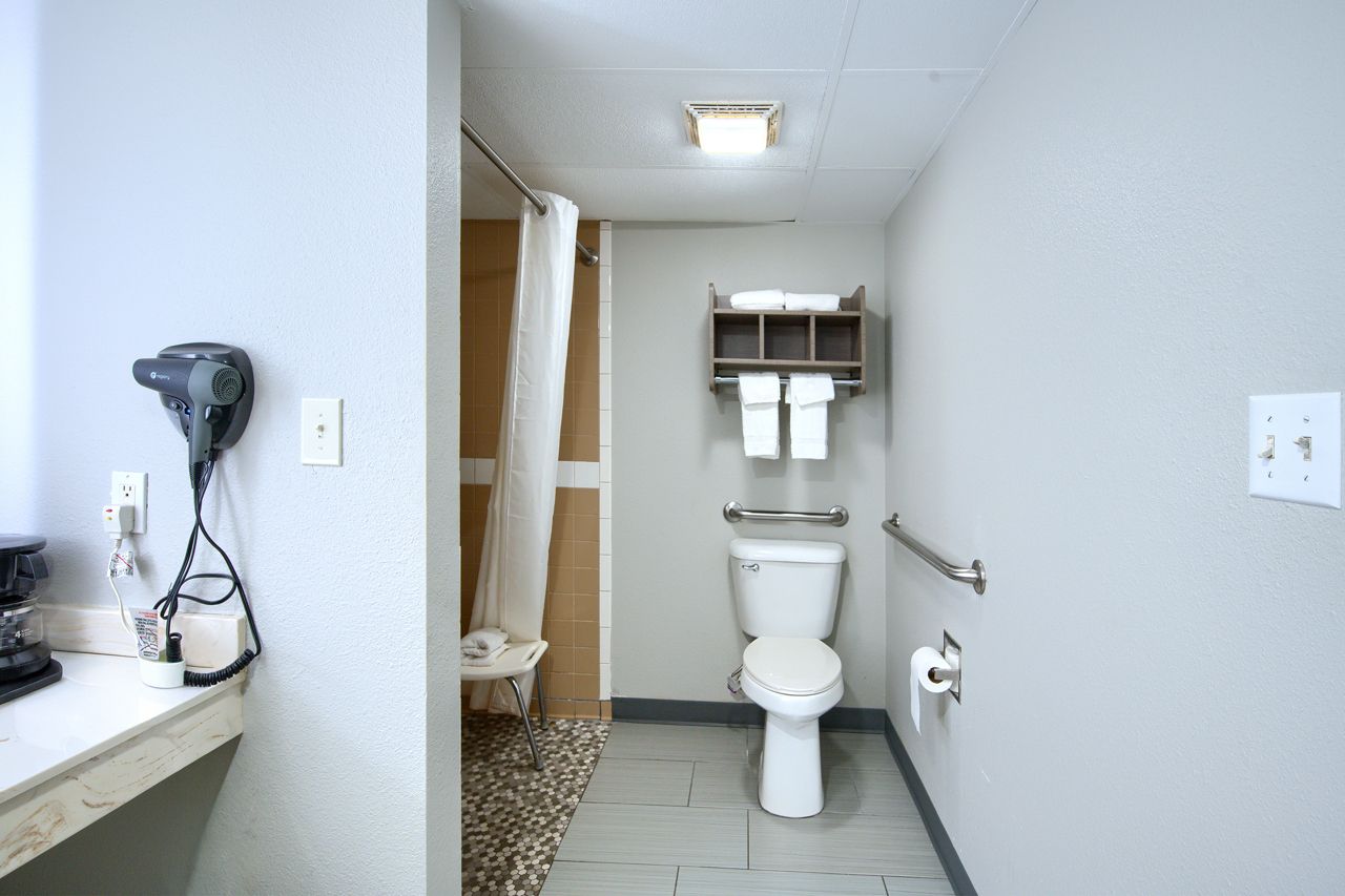 Bathroom with shower, toilet, and vanity. Gray walls, handrail, towel rack, and hair dryer.