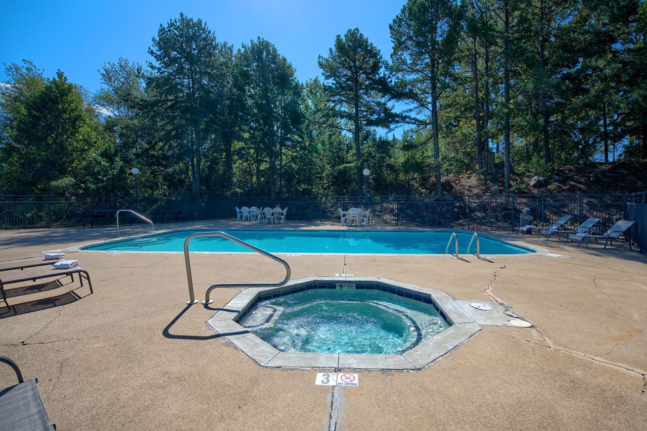 Pool and jacuzzi surrounded by concrete, trees in background, sunny day.