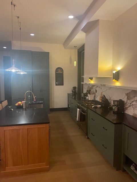 Modern kitchen with green cabinets, black countertops, wood island, and marble backsplash.