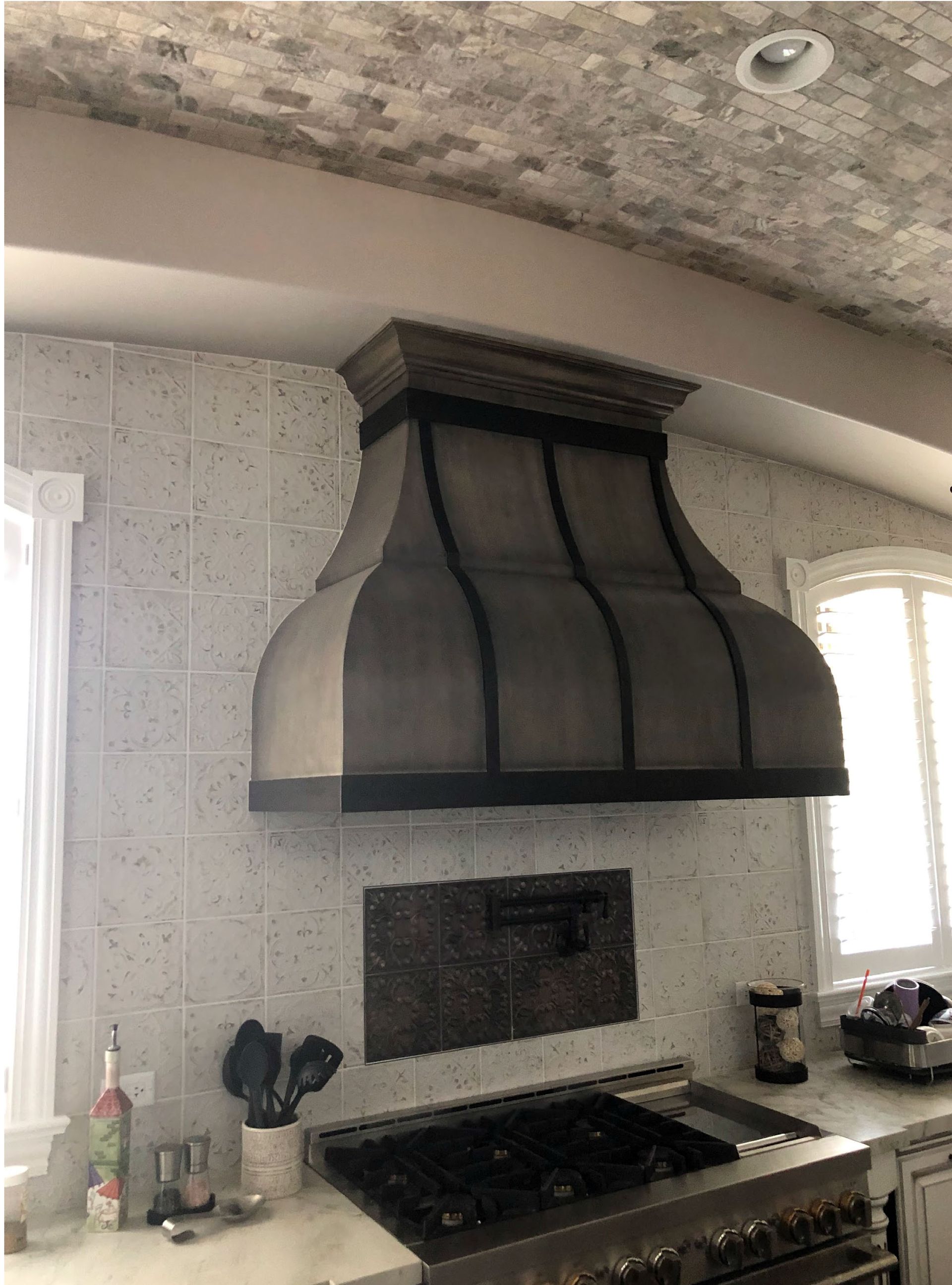 Kitchen with stainless steel range hood above a gas stove, white tiled backsplash and ceiling.