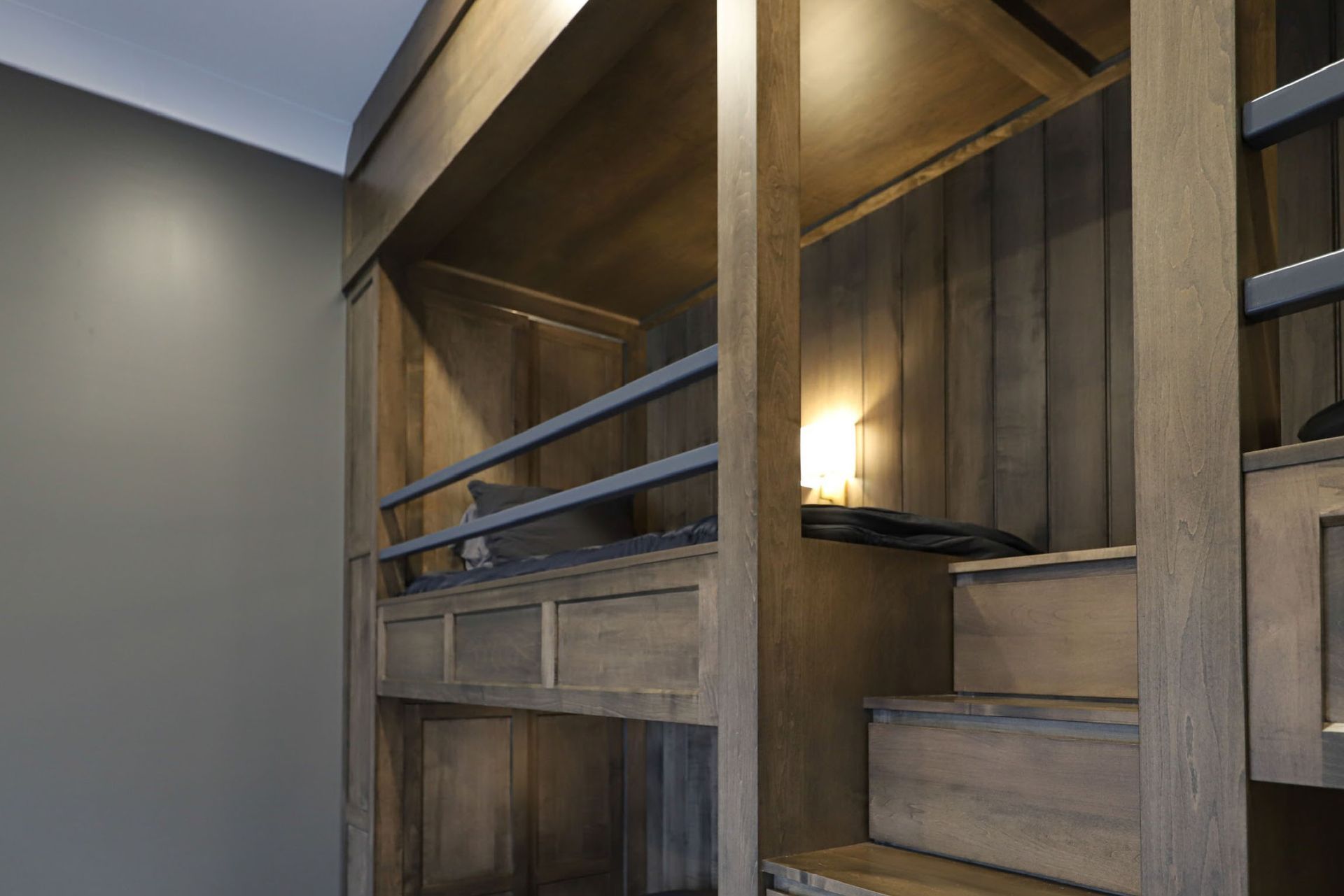 Wooden bunk bed with stairs, shelving, and a small light fixture.