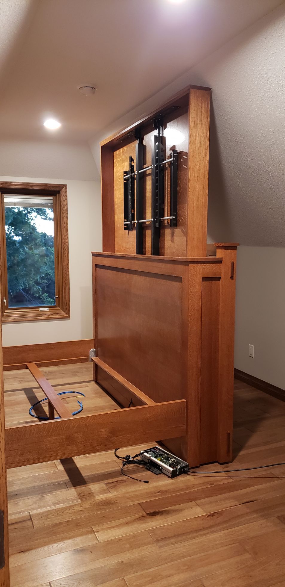 A wooden bed frame with a large headboard, a TV lift, and a window.