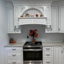 White kitchen with cabinets, stove, and a decorative hood, with fall decor.
