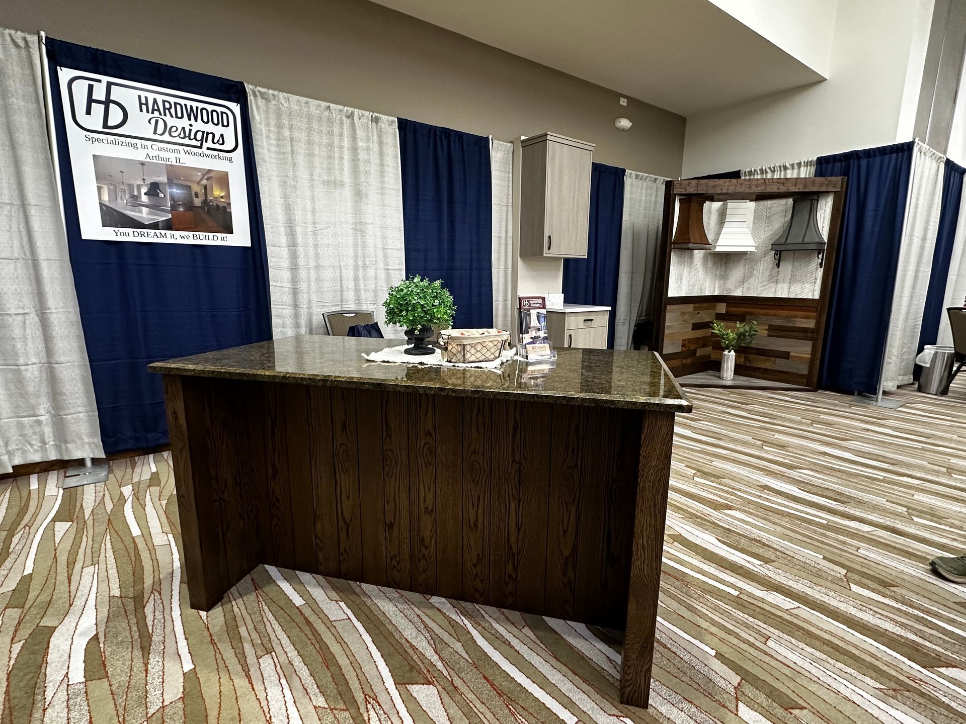 Exhibition booth with a wood kitchen island and cabinetry. Dark blue and white curtains in background.