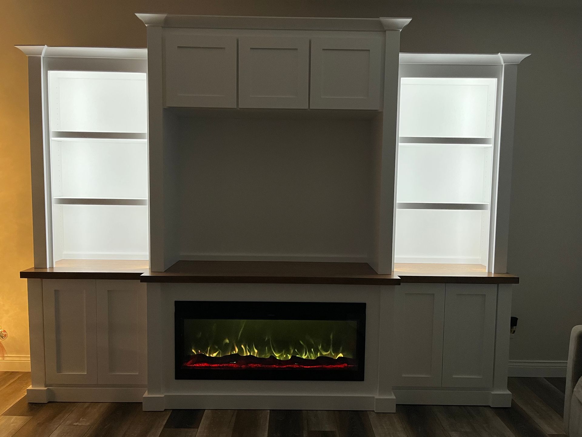 White built-in entertainment center with a fireplace, open shelves with interior lights, and cabinet doors.