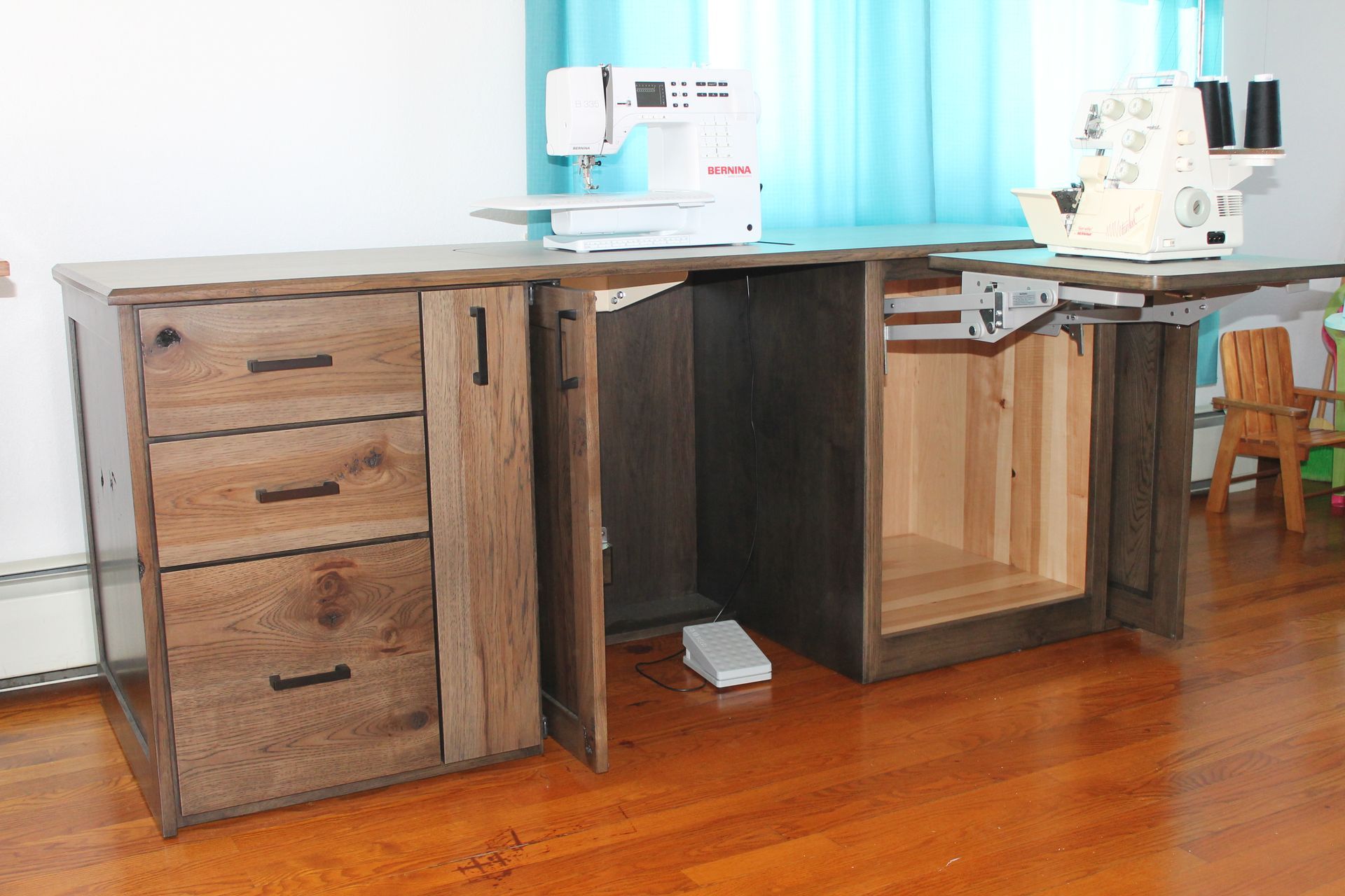 Wooden sewing table with drawers and folding extensions, holding sewing machines.