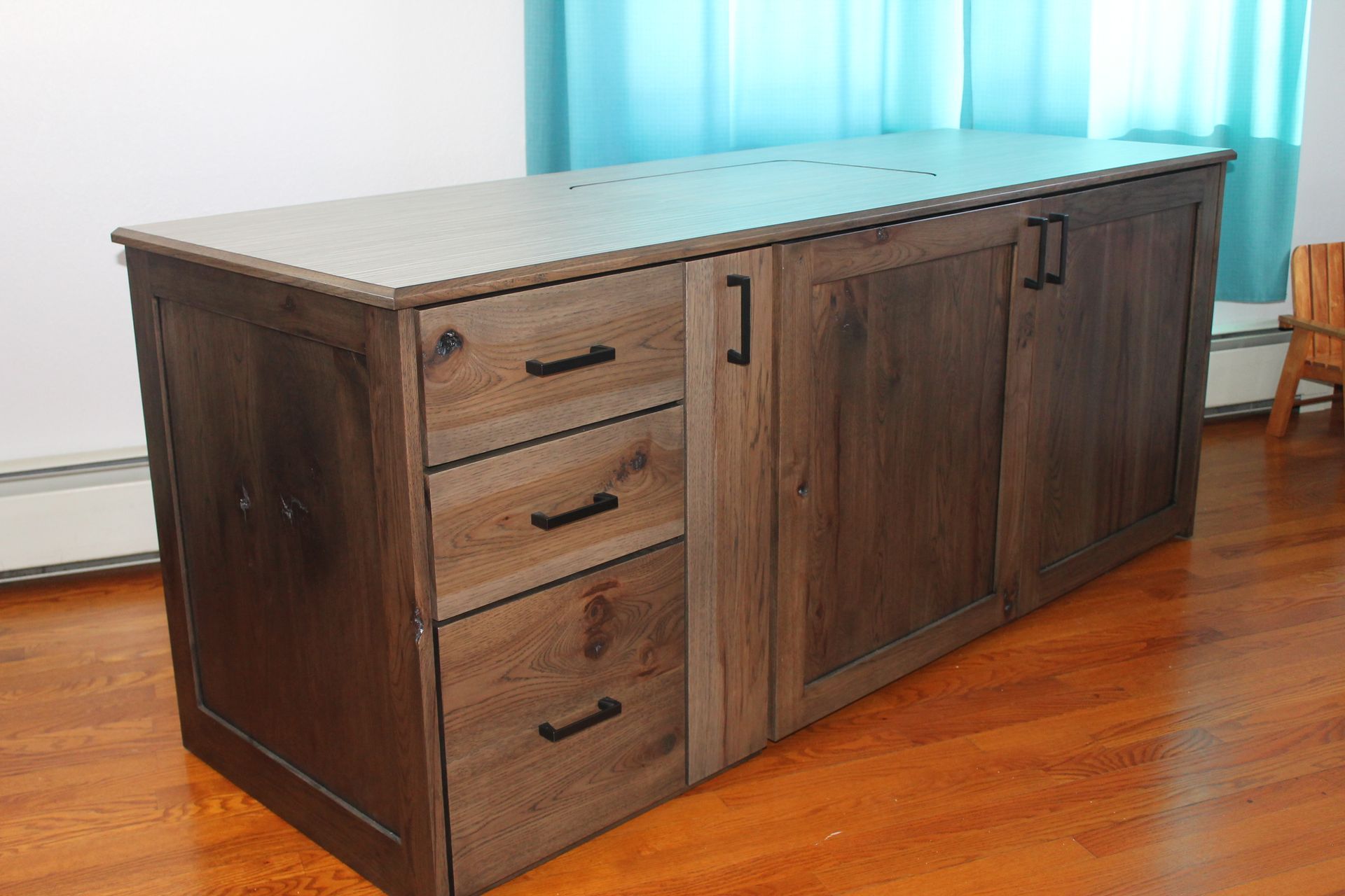 Wooden desk with drawers and cabinet doors, set on a hardwood floor, with a light blue curtain in the background.