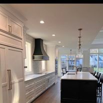 Modern kitchen with white cabinetry, black island, range hood, and wood floors.