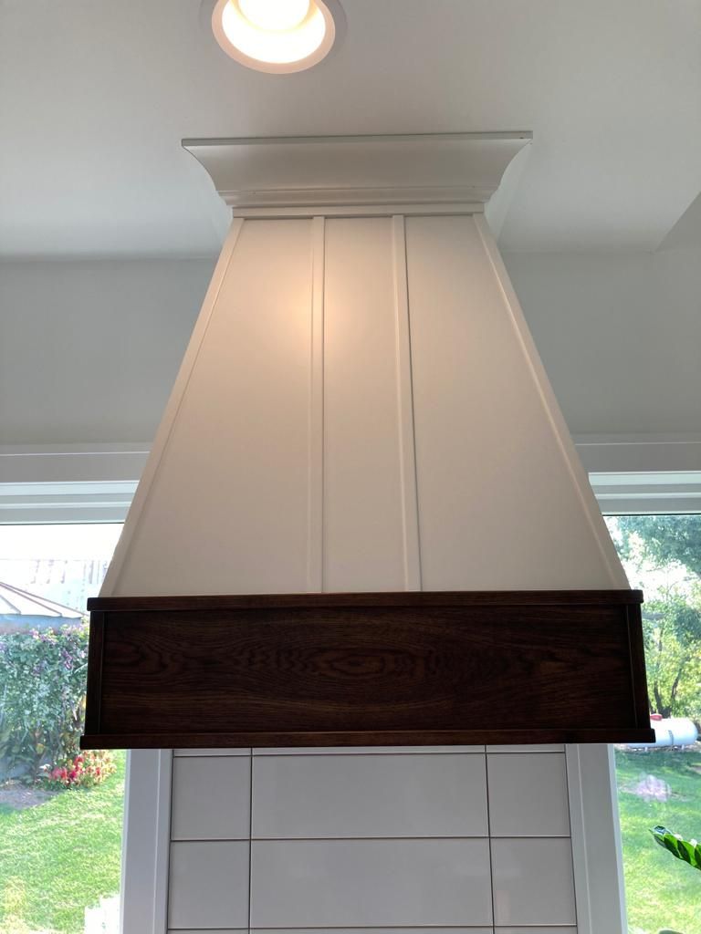White and dark wood range hood in a kitchen with a window and trim.