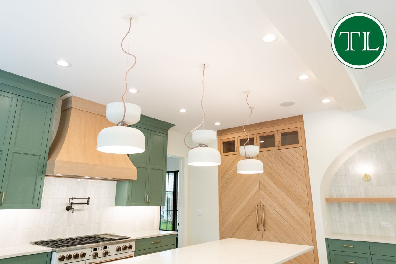 Green and wood-toned kitchen with white pendant lights and a white countertop island.
