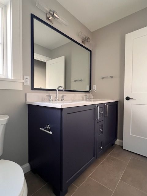 Bathroom with navy blue vanity, white countertop, large mirror, and neutral walls.