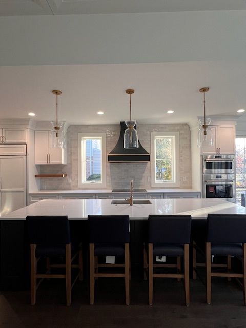 Spacious kitchen with dark blue island, white countertops, and gold pendant lights. Dark wood floors and windows.
