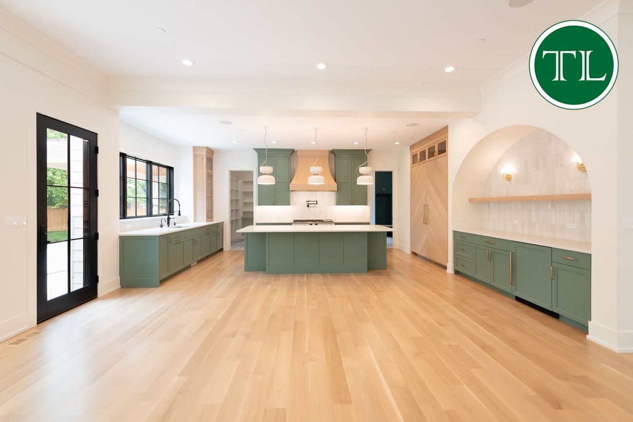 Spacious, light-filled kitchen with sage green cabinets, light wood floors, and arched doorway.