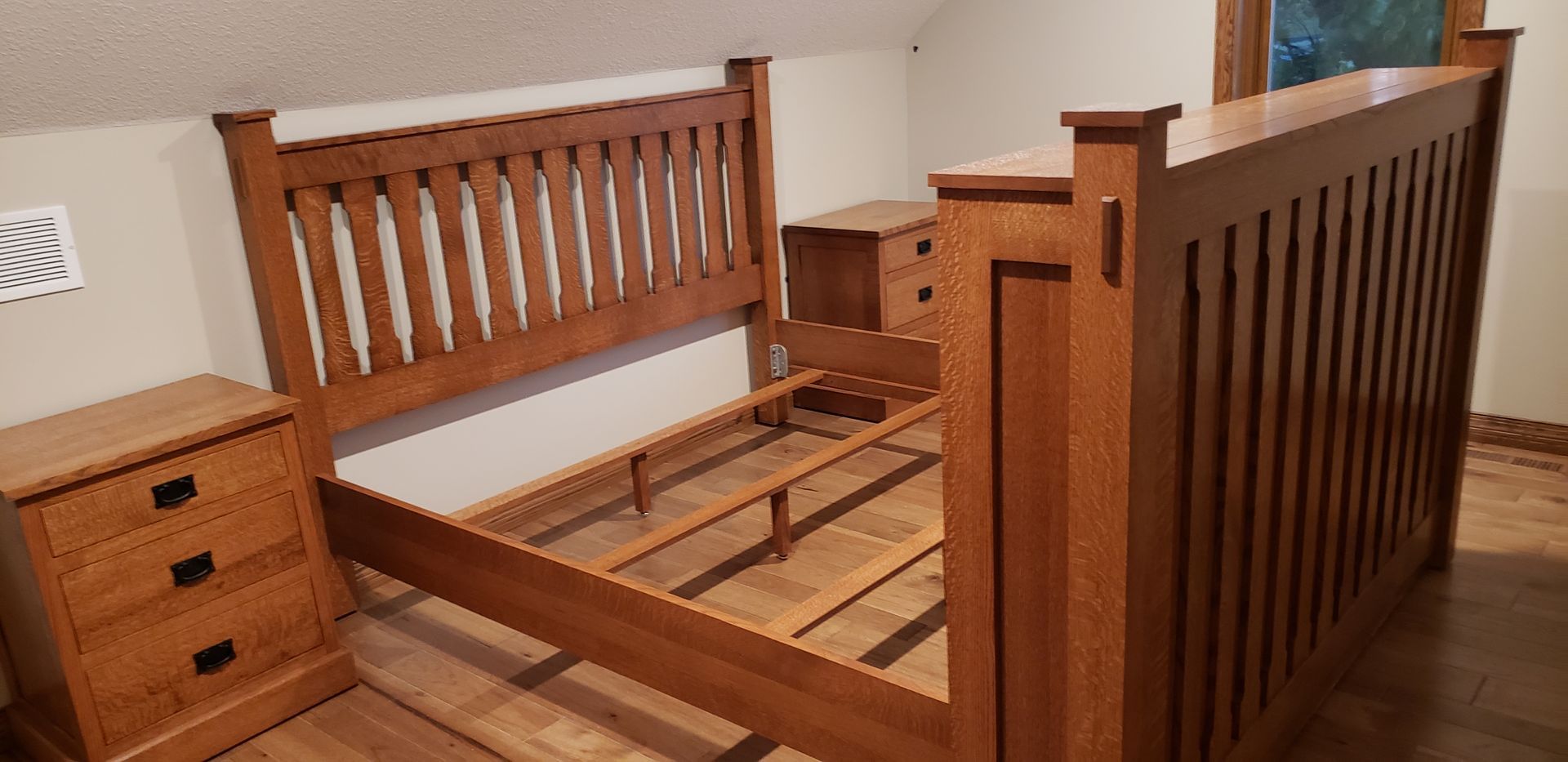 Wooden bed frame with headboard, footboard, and two nightstands in a bedroom.