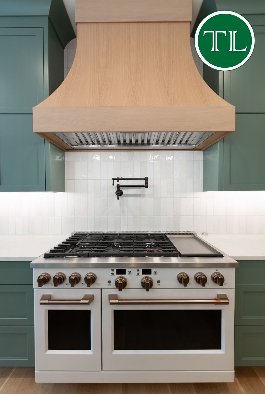 White kitchen range with matching hood, green cabinets.
