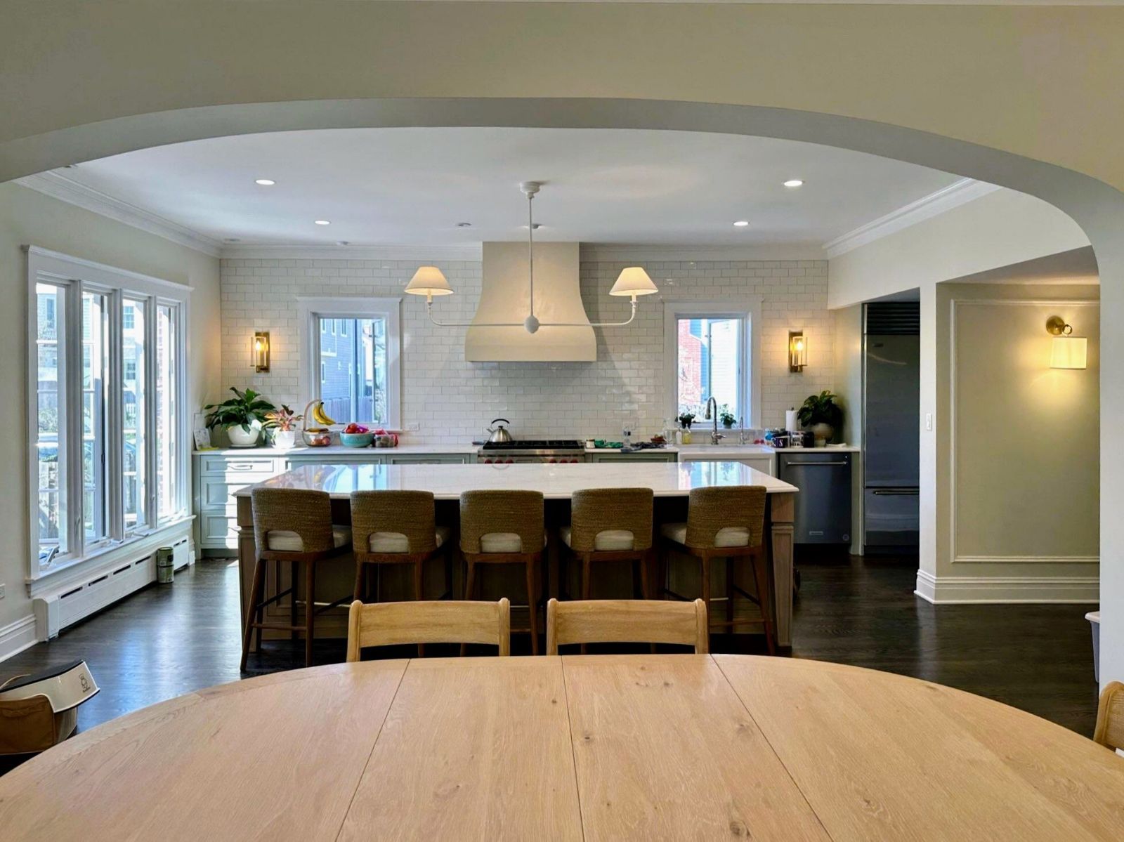 Spacious kitchen with a large island, stools, white cabinets, and an arched doorway.
