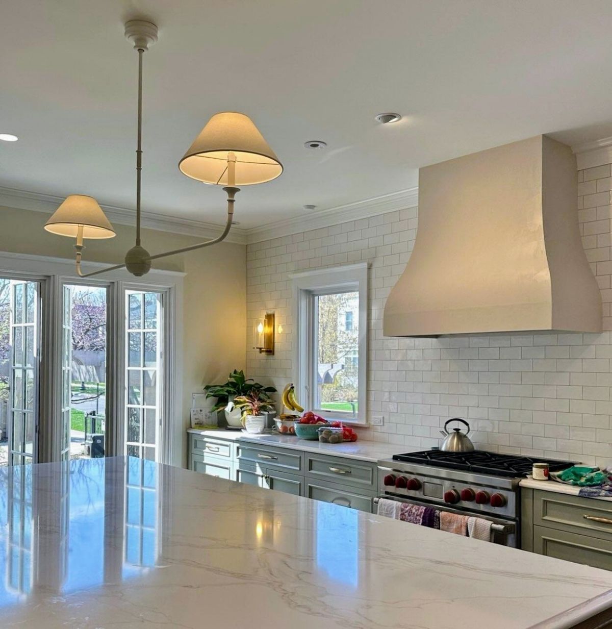 Kitchen with white cabinetry, marble countertops, and a stove under a hood.