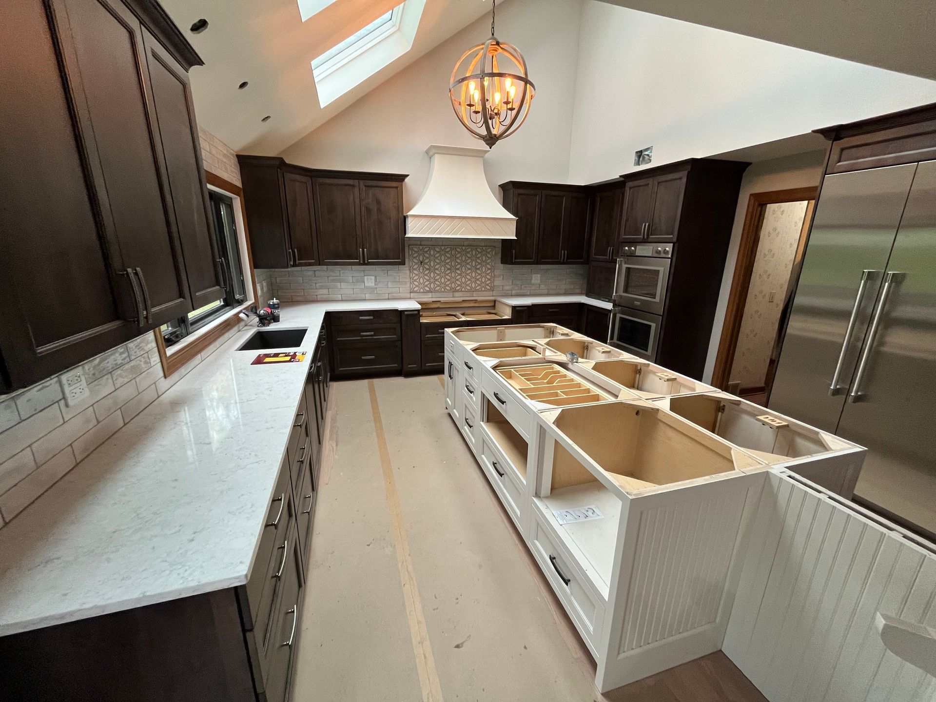 Kitchen renovation with dark brown cabinets, white countertops, island, and beige range hood.