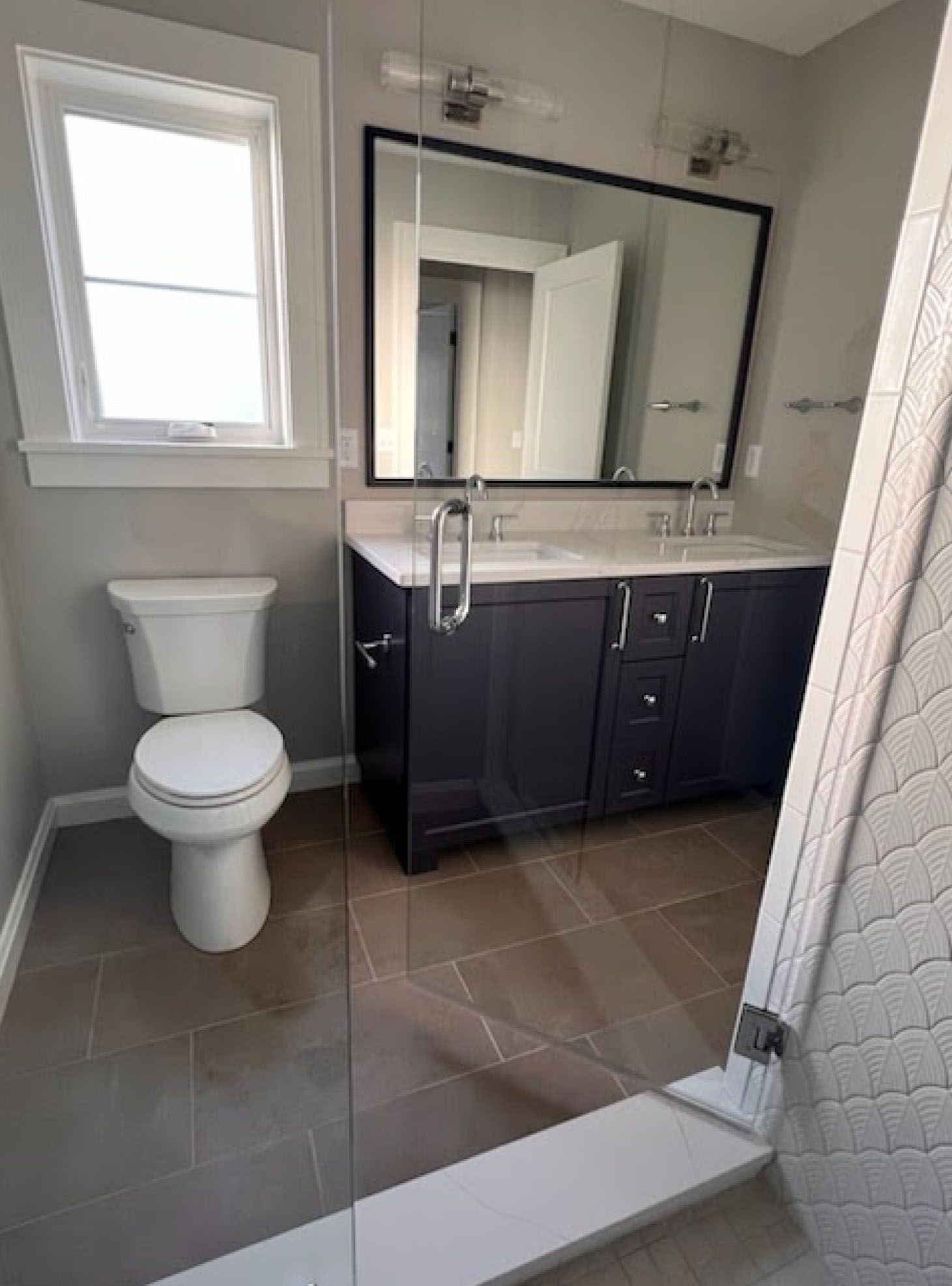 Bathroom with blue vanity, large mirror, toilet, window, and glass shower door.