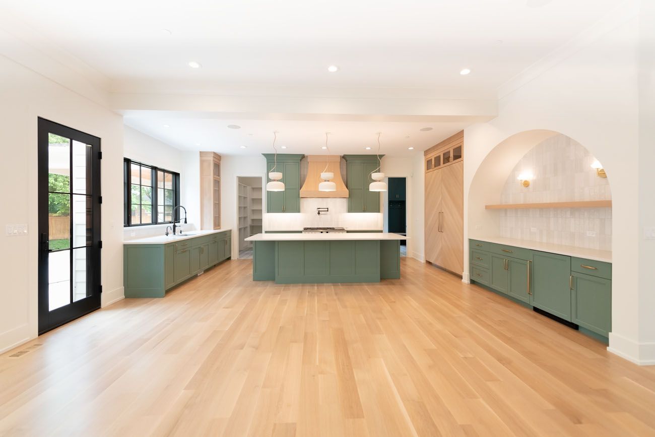 Open kitchen with green cabinets, light wood floors, and arched doorway.