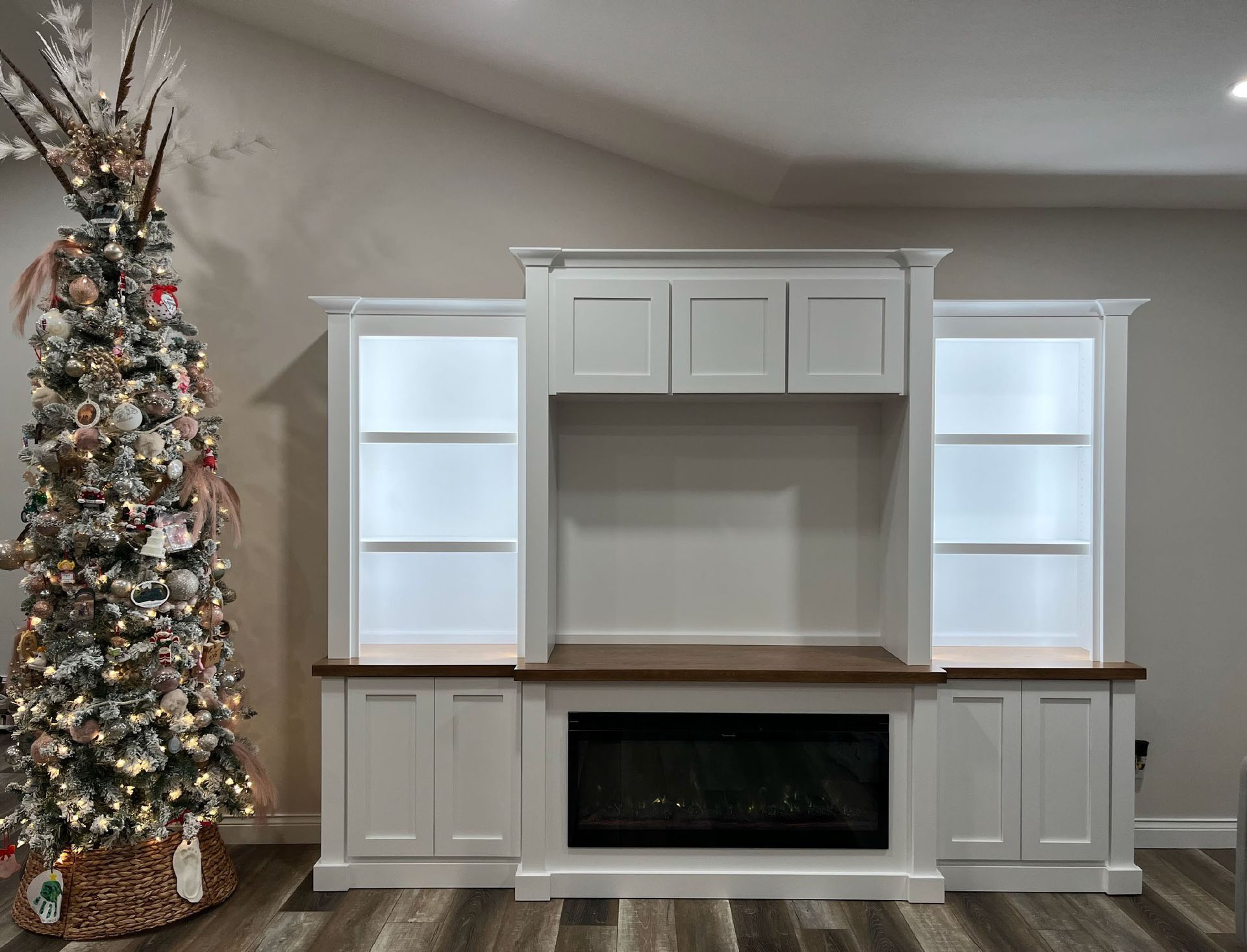 Built-in white media center with fireplace and shelves, next to decorated Christmas tree.
